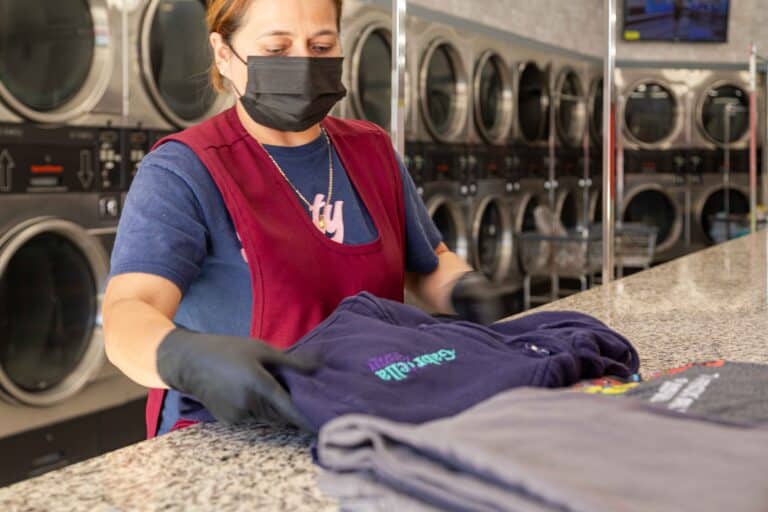 Woman folding clothes while wearing a face mask and gloves at 24/7 laundry near USC